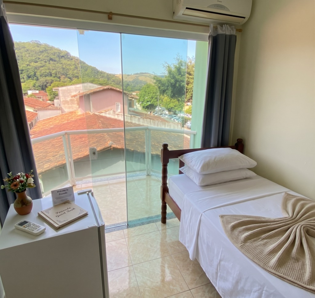 Quarto com cama de solteiro, varanda com vista para as montanhas e frigobar